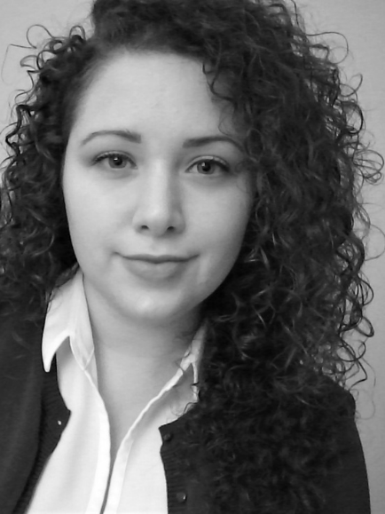 Black and white photograph of Emily Cain, with curly brown hair, wearing a blazer and dark shirt.