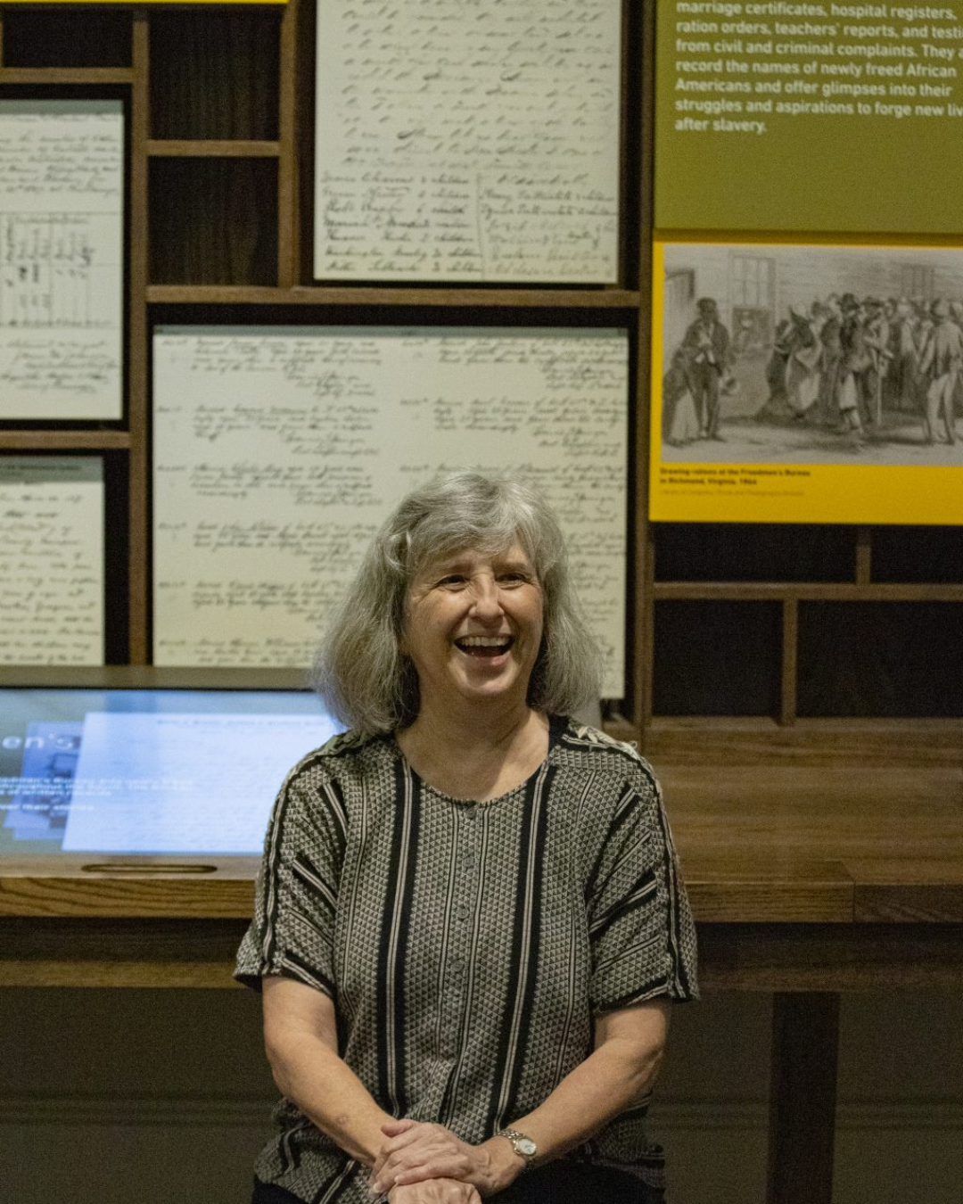 Photograph of TC volunteer Jennie Caughran laughing while being interviewed in the Freedmen's Bureau section of the 2022 "Make Good the Promises: Reconstruction and Its Legacies" exhibition at NMAAHC.