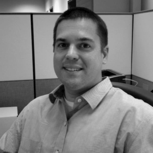 Paul Day, wearing a button down shirt and seated at a desk.